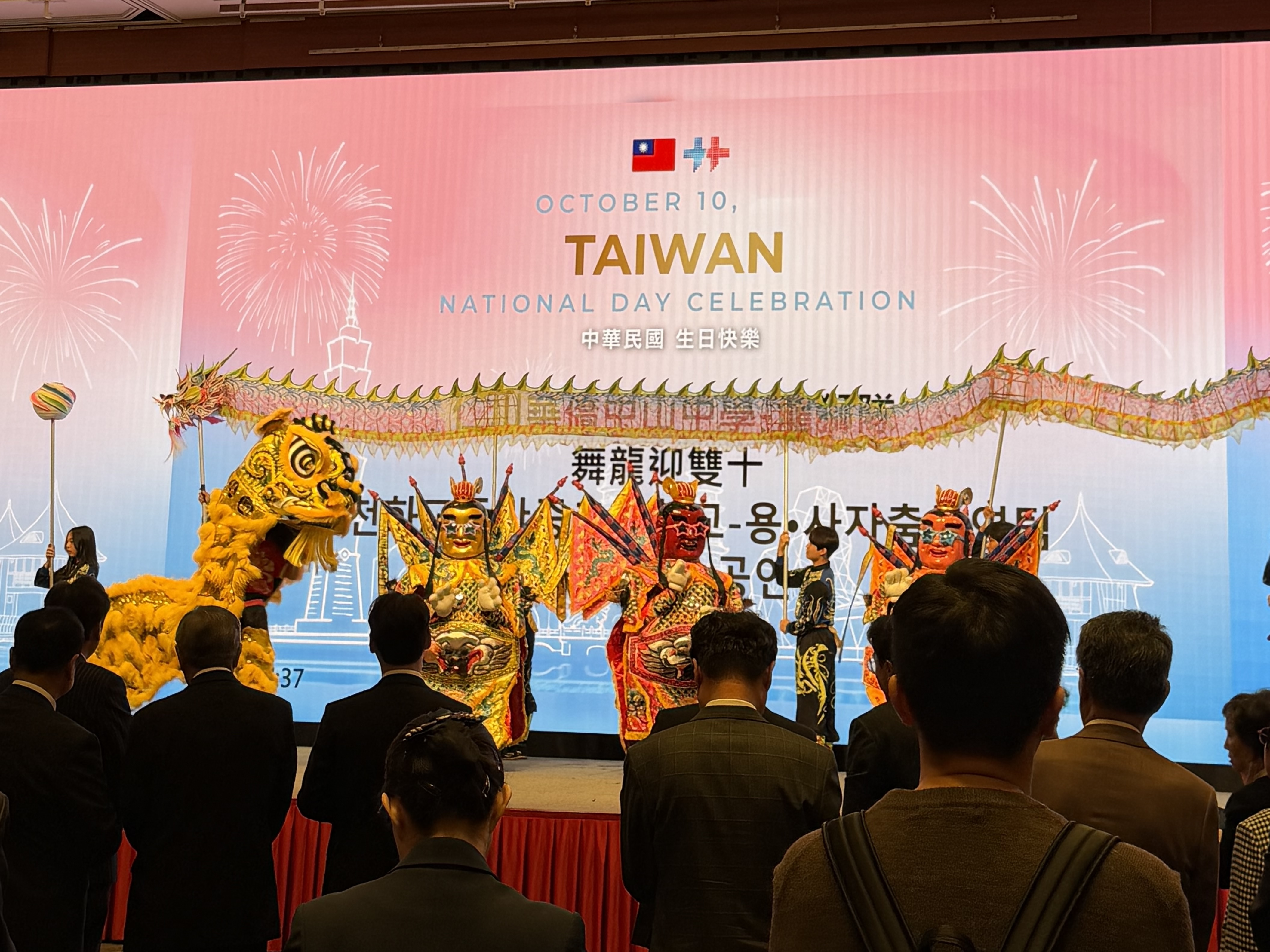 A lion dancer and Nezha performers on stage at the 2026 Double Ten Day Celebration, viewed by reception guests.